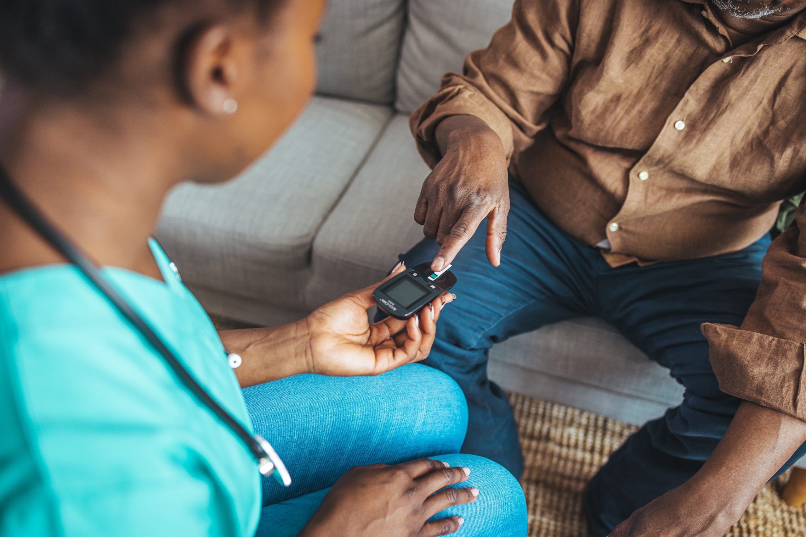 Senior diabetic man is having a check up at home from a district nurse. She is checking his blood glucose levels. Home Diabetes Treatment. Female nurse and patient doing a glucose test